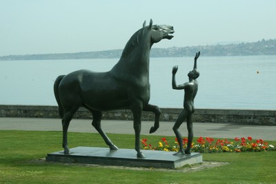 Escultura de caballo con nio en los jardines de Ginebra con el lago Leman al fondo.
